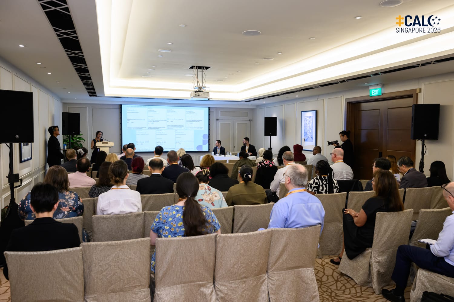 Ms Nina Ding speaks at the podium during a breakout session at the Conference, with Mr Daniel Baird and Mr Pasha Peyrovi seated at a table nearby at The Fullerton Hotel Singapore.
